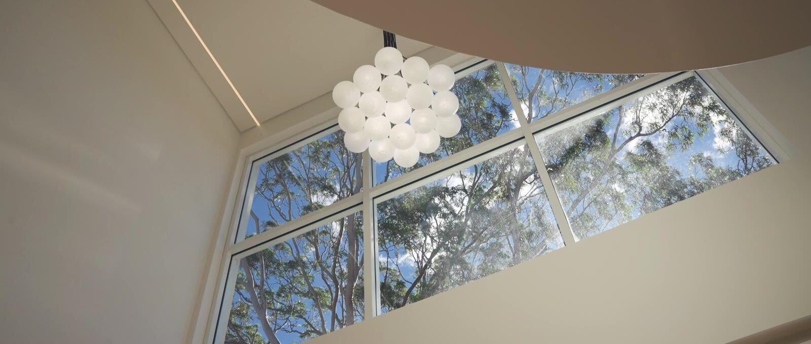 Raked skylight window with sculptural pendant light and treetop views