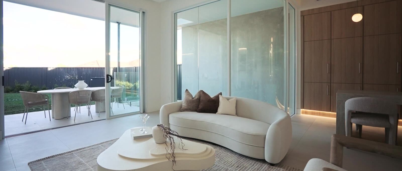 Living room with curved sofa, glass walls and timber joinery at dusk